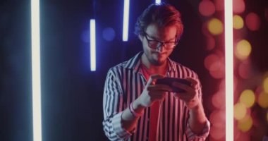 Orta Doğulu kaygısız bir adamın neon arka planda akıllı telefonuyla video oyunu oynaması. Modern teknoloji ve eğlence konsepti.