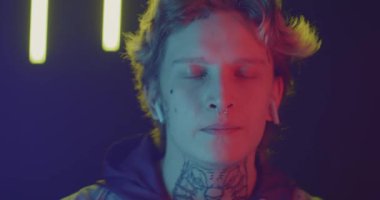 Kulaklık takan genç bir adamın yakın plan portresi. Geceleri müzik dinlerken arka planda neon ışığı var. Gençlik yaşam tarzı ve rahatlama konsepti.