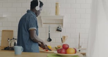 Afro-Amerikalı öğrenci yemek pişirip salata yapıyor ve kulaklıkla müzik dinliyor. Halk ve gençlik kültürü kavramı.
