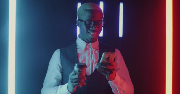 非洲裔美国商人的肖像 使用智能手机 喝着咖啡 在黑暗的空间与霓虹灯照明 现代技术和企业生活方式概念 — 图库视频影像