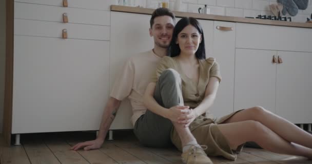 一对快乐的年轻夫妇坐在厨房的地板上 微笑着看着相机 住宿和家庭生活方式概念 — 图库视频影像