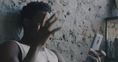 Afro-Amerikalı mutlu bir adamın portresi. Akıllı telefonuyla video görüşmesi yapıyor. Evde yatakta konuşuyor ve el kol hareketi yapıyor. İletişim ve boş zaman kavramı.