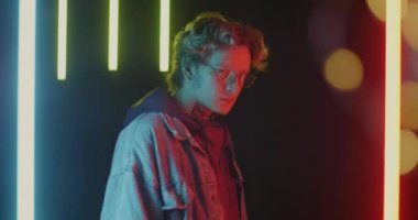 Erkek öğrencinin kameraya dönüp fütürist neon arka planda gözlüğe dokunması. Zeki insanlar ve gençlik tarzı konsepti.