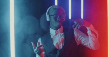 Neon ışıklı arka planda dans eden kulaklık takan Afro-Amerikan işadamının yavaş çekim portresi. Eğlence ve teknoloji konsepti.