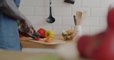 Bıçaklı erkek eli yemek hazırlıyor. Modern evdeki mutfakta salata için sebze kesiyor. Afro-Amerikalı adam organik malzemelerle sağlıklı yemek pişiriyor..