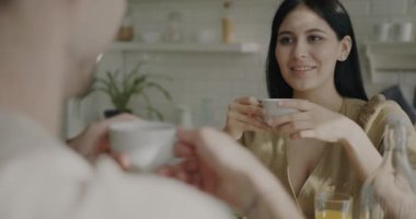 Evde keyifli bir kahvaltı yaparken kahve içen ve kocasıyla konuşan neşeli genç bir kadın. Boş zaman aktivitesi ve aile hayatı konsepti.