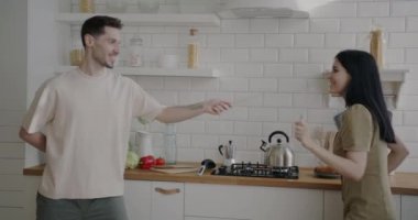 Genç adam, neşeli karısıyla eskrim oynuyor mutfakta eğleniyor. Gençlik yaşam tarzı ve ilişki kavramı.