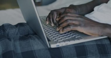 Tasasız Afrikalı Amerikalı bir adamın dizüstü bilgisayarla yazı yazarken ve evde gülerken çekilmiş portresi. Çevrimiçi eğlence ve modern teknoloji kavramı.