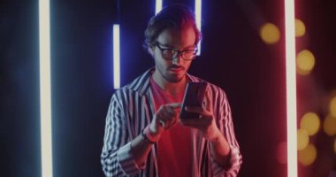 Orta Doğulu bir adamın portresi akıllı telefon kullanıyor ekranlara dokunuyor ve bokeh ışıklarıyla neon arka planda gülüyor. Modern teknoloji ve iletişim konsepti.