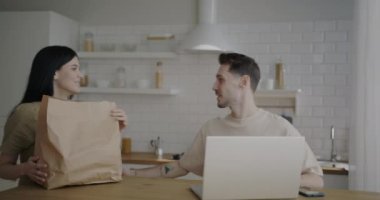 Genç bir kadın eve gelip kocasını öpüyor. Kese kağıdından yiyecek çıkarıyor. Mutfakta erzakları tartışıyor. Alışveriş ve aile hayatı konsepti.