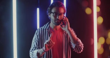 Cep telefonuyla konuşan neşeli Orta Doğulu bir adamın portresi. Neon arka planda el gülüşü ile üçe kadar sayıyor. İletişim ve gece hayatı kavramı.