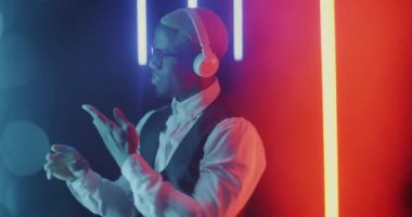 Çok renkli neon arka planda kulaklık kullanarak dans eden neşeli genç iş adamının yavaş çekim portresi. Mutlu insanlar ve gelecekçi uzay konsepti.