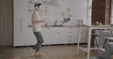 Genç adam kahve içip dans ediyor ve evde kulaklıkla müzik dinliyor. Ev hayatı ve eğlence anlayışı.
