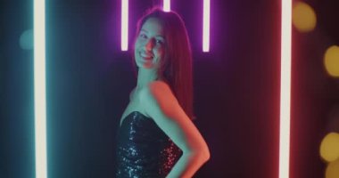 Güzel neon arka planda kameraya gülümseyen süslü elbiseli çekici genç bir kadının portresi. Kadın güzelliği ve cazibe konsepti.