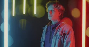 Erkek öğrencinin dumanı tüttürmesi ağır çekimde. Çok renkli neon arka planda tek başına duruyor. Gençlik yaşam tarzı ve kötü alışkanlık kavramı.