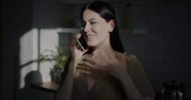 Cep telefonuyla sohbet eden neşeli bir kadının portresi. Mutfakta gün ışığıyla aydınlanan yüzüyle duygularını paylaşıyor. İnsanlar ve iletişim konsepti.