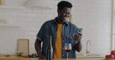 Afro-Amerikalı bir adamın portresi akıllı telefonuyla çevrimiçi video görüşmesi yapıyor evde el sallayarak konuşuyor. İletişim ve aygıt kavramı.