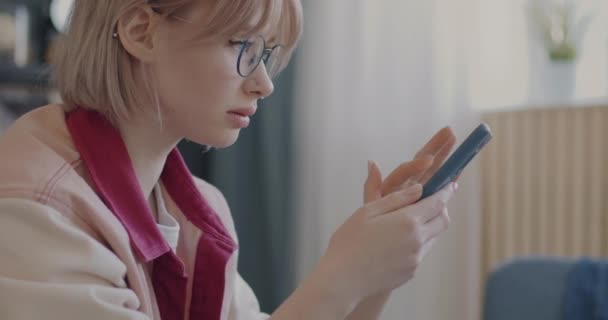 アパート内のディスプレイを見ながらスマホアプリを使っている女子学生 現代のガジェットやソーシャルメディアコミュニケーションの概念 — ストック動画