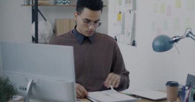 Modern cam duvar ofisinde masa başında çalışan genç bir uzmanın portresi. İş ve mali evrak kavramı.