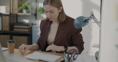 Ofiste tek başına çalışan, dizüstü bilgisayarı kullanan ve finansal bilgiler yazan bir kadın. İş ve modern teknoloji kavramı.
