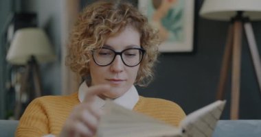 Kitap okuyan ve modern dairede boş zamanlarında gülümseyen zeki genç bir kadının portresi. Akıllı insanlar ve edebiyat konsepti.