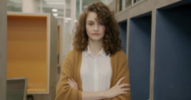 Ciddi bir yüzle ofiste kameraya bakan kararlı genç bir iş kadınının ağır çekimde portresi. İnsanlar ve çalışma alanı kavramı.