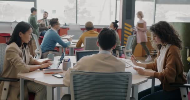 オープンスペースのオフィスでは 男性と女性の従業員の多様なグループがデスクに座って話しています 企業生活と日常の概念 — ストック動画