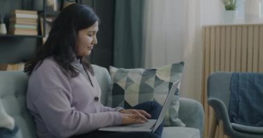 Dizüstü bilgisayarla çalışan genç bir kadının portresi sonra kapanıyor ve evdeki kanepede rahatça gülümsüyor. İnsanlar ve modern teknoloji kavramı.