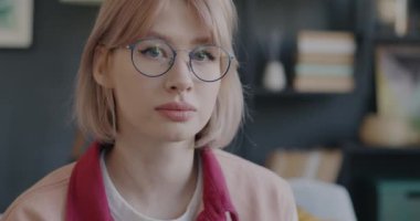 Moda gözlük takan, saçlara dokunan ve evde gülümseyen neşeli bir kızın portresi. Olumlu duygu ve tasasız milenyum konsepti.