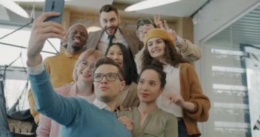 Neşeli meslektaşlar akıllı telefon kamerasıyla selfie çekiyorlar modern çalışma alanında el hareketleriyle poz veriyorlar. Gençlik ve iş kavramı.