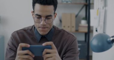 Genç bir çalışanın portresi video oyunu oynuyor. Mola sırasında akıllı telefon kullanarak rahatlıyor. Eğlence ve modern teknoloji konsepti.
