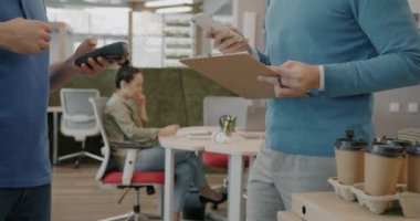 Ofisteki akıllı telefondan yemek siparişini ödeyen iş adamlarının yakın çekimleri. Yanında üniformalı bir kurye duruyor..