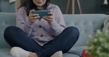 Evde zaferi kutlamak için akıllı telefon kullanarak video oyunu oynayan kaygısız kadın. Modern teknoloji ve eğlence konsepti.