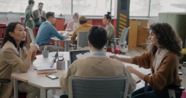 Çok ırklı iş adamlarından oluşan bir grup çalışma sahasında çalışıyor ve masalarda oturup konuşuyorlar. İşbirliği ve işyeri konsepti.