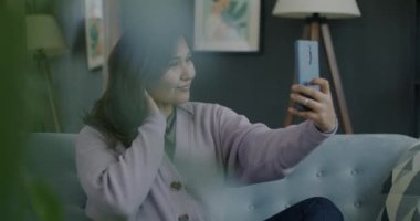 Evde akıllı telefon kamerasıyla selfie çeken mutlu Asyalı kadın portresi. Modern yaşam tarzı ve fotoğraf konsepti.