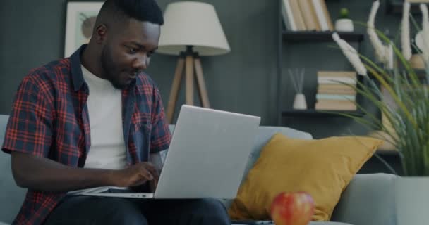 自宅の入力からノートパソコンで作業する若い男のフリーランスの肖像画ソファだけで座っている リモートジョブと現代的な技術コンセプト — ストック動画