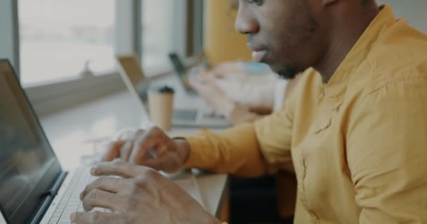 用手提电脑打字与同事坐在同一办公室的办公桌旁 对有野心的非洲裔美国员工进行特写镜头 商业和现代技术概念 — 图库视频影像