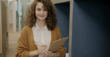 İş yerinde yalnız başına kameraya bakarak gülümseyen modaya uygun giyinmiş neşeli genç bir bayan portresi. Milenyum ve iş kavramı.