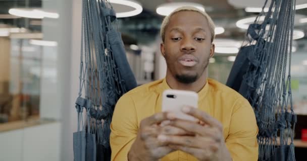 Alegre Empleado Afroamericano Está Utilizando Teléfono Inteligente Sonriendo Sentado Tumbona — Vídeo de stock