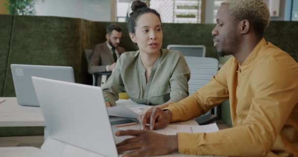 アフリカ系アメリカ人従業員はラップトップを使用しており オープンスペースオフィスの女性同僚と話しています ビジネスコミュニケーションと現代技術の概念 — ストック動画