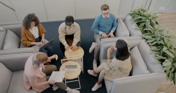 若い野心的なビジネスマンの高い角度から見た創造的なチームは 現代のオフィスで座って話をするアイデアを議論します 若者とキャリアの概念 — ストック動画
