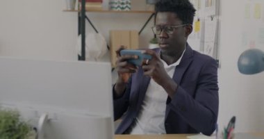 Ofisteki masada akıllı telefonla online video oyunu oynayan neşeli iş adamının portresi. Modern teknoloji ve eğlence iş kavramında.