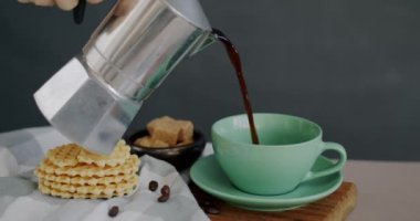 Gri arka planda nefis waffle 'ların yanında demlikten fincana dökülen kahvenin yakın çekimi. Tatlı ve öğle yemeği konsepti.