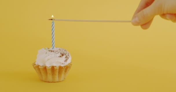 在黄色背景的纸杯蛋糕上用女性手点燃蜡烛的特写 生日蛋糕和节日庆祝的概念 — 图库视频影像