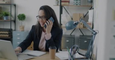 İş kadını cep telefonuyla konuşuyor bilgisayarla konuşuyor ve ofiste yazıyor. Kurumsal iletişim ve iş insanları kavramı.