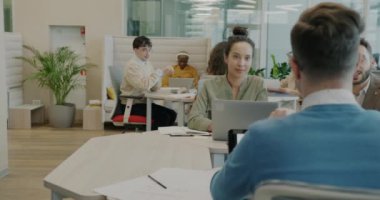 Çalışan bir grup erkek ve kadın modern açık uzay ofisinde masalarda birlikte oturan cihazları kullanarak konuşuyorlar. İş ve işyeri kavramı.