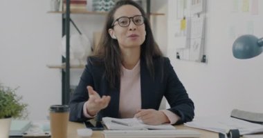 Orta Doğulu bir çalışanın iş yerindeki video görüşmesi sırasında ortağıyla konuştuğu portre. Takım elbiseli genç bayan kulaklık takıyor kameraya bakıyor ve konuşuyor..