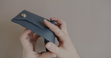 Boş cüzdanı açıp bej rengi arka planda para arayan ellerin yakın çekimi. Fakir kişi mali sorun ve yoksulluk çekiyor.