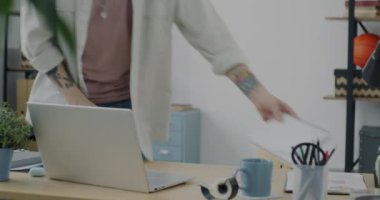 Yaratıcı bir çalışan sabah ofise gelip masa başında dizüstü bilgisayarla çalışıyor. Modern teknoloji ve kariyer kavramı.