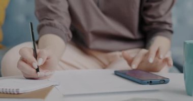 Akıllı telefon kullanan ve evdeki kağıtlara notlar yazan kadınların yakın çekimleri. Modern teknoloji ve iş evrakları kavramı.